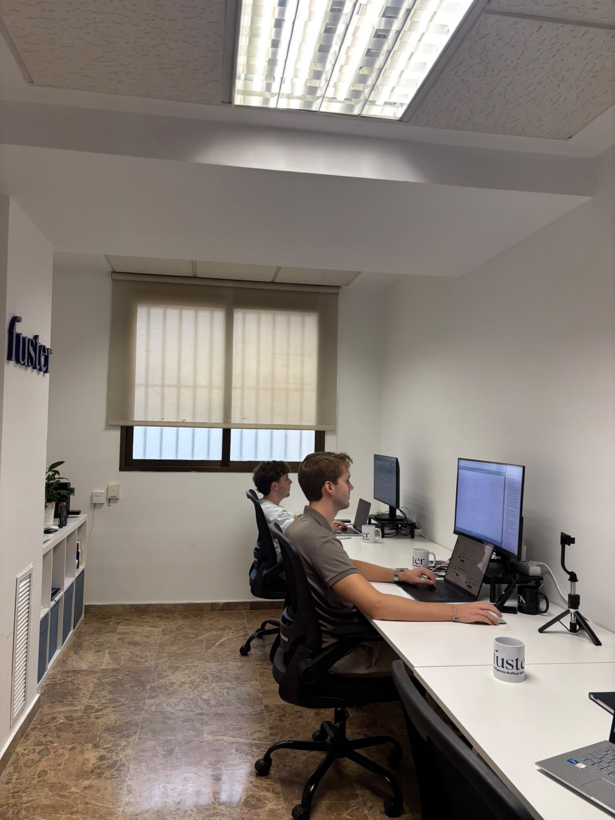 Equipo de Fuster Agencia trabajando en la oficina de Valencia junto al logotipo de la agencia